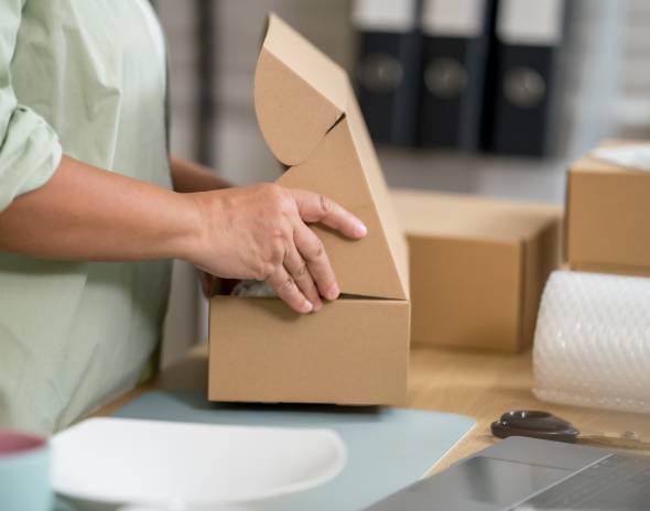 Hands packing cardboard shipping box with bubble wrap